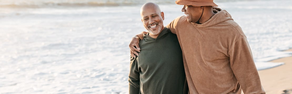 Male couple walks along the beach while holding each other.